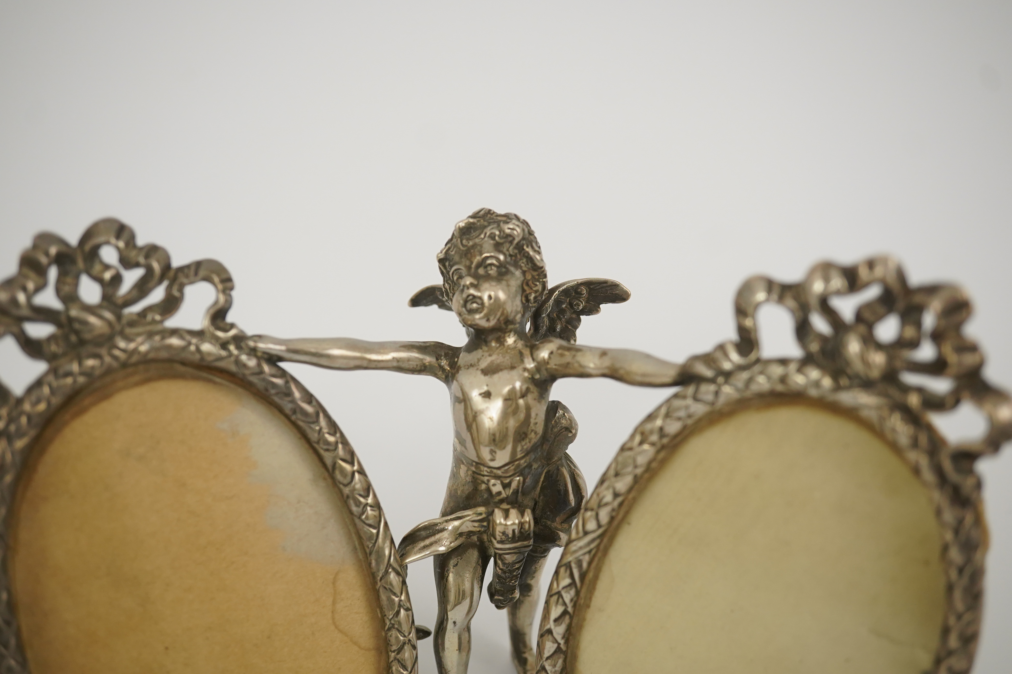 A late 19th century Hanau silver double oval photograph frame, supported by central figure of Cupid, by Berthold Muller